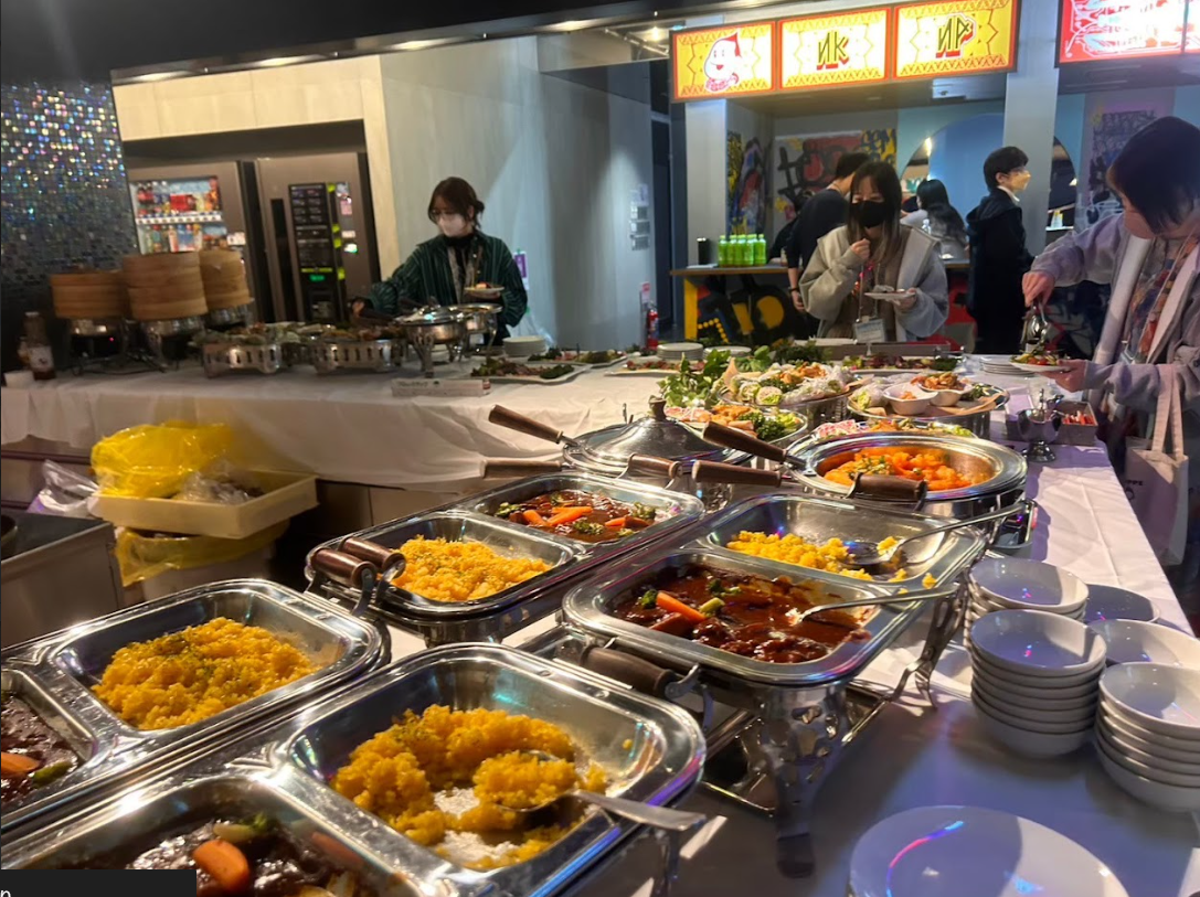 温かい料理が並ぶビュッフェコーナーで料理を取る参加者